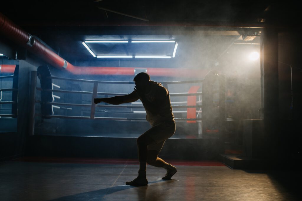 A male boxer is boxing with a shadow on the background of a boxing ring.